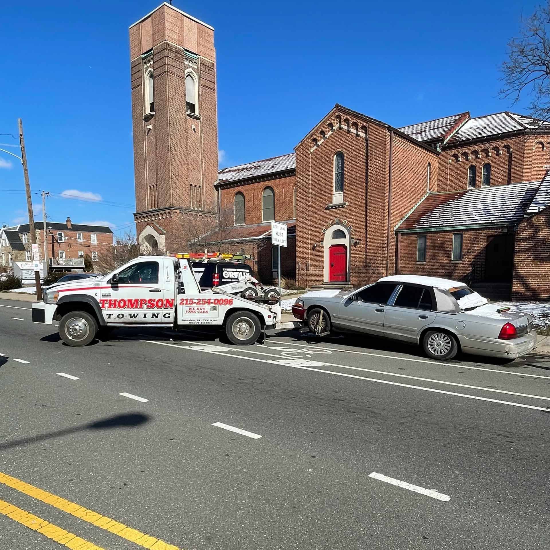 A tow truck from Thompson towing is towing a car in front of a church.