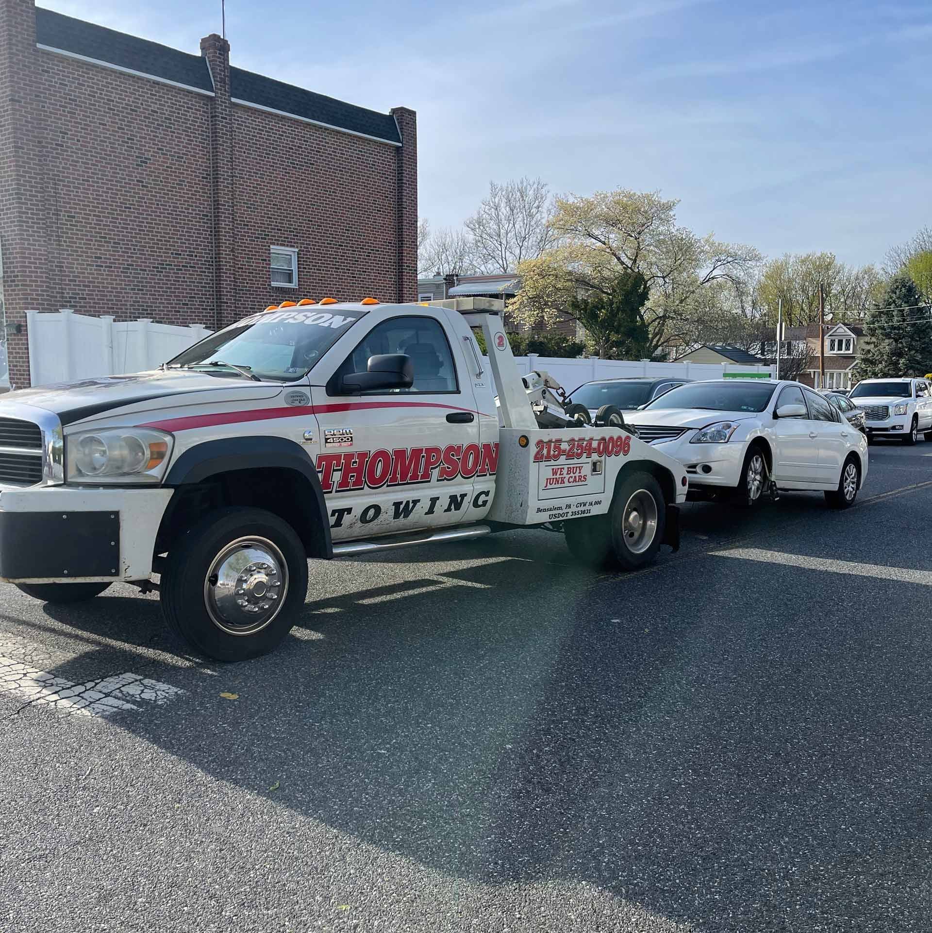A white tow truck from Thompson Cash is towing a white car.