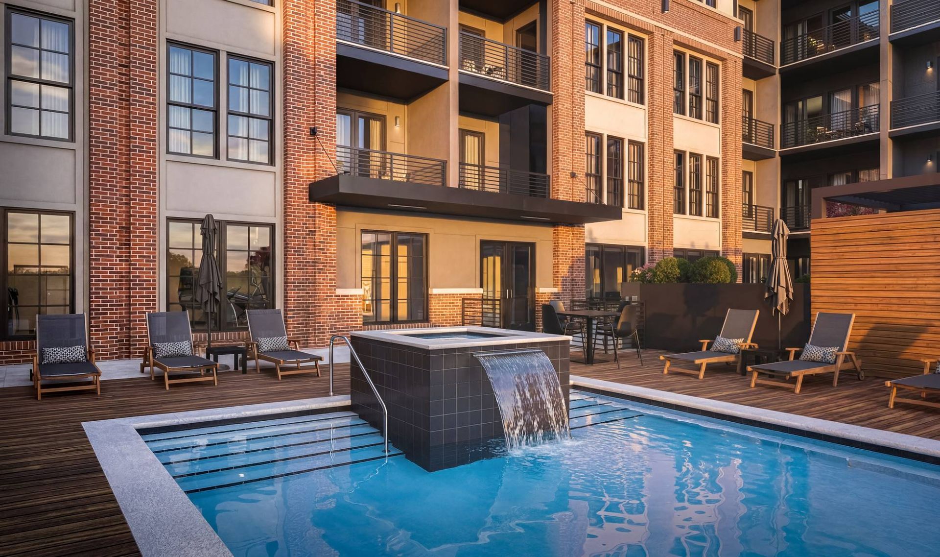 Outdoor community pool with lounge chairs and brick building backdrop.