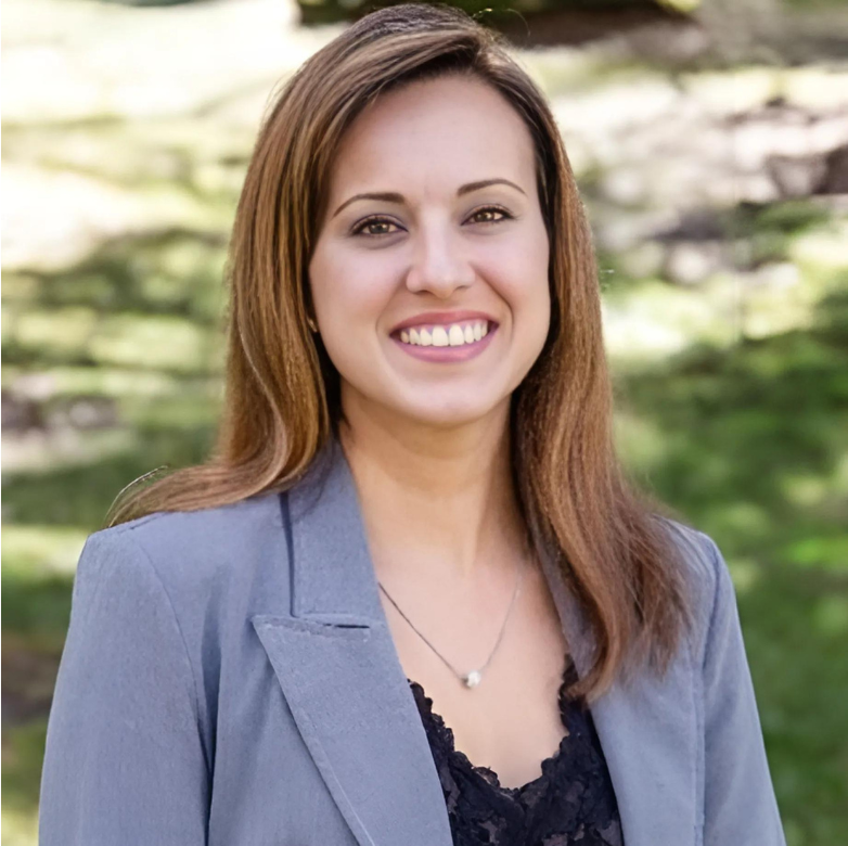 A woman in a grey jacket and black top is smiling for the camera.