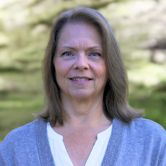 A woman wearing a gray sweater and a white shirt is smiling for the camera.