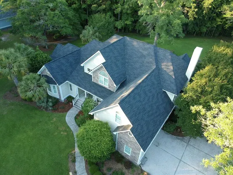 An Aerial View Of A Large House With A Blue Roof Surrounded By Trees — Summerville, SC — Palm & Pineapple Roofing and Exteriors
