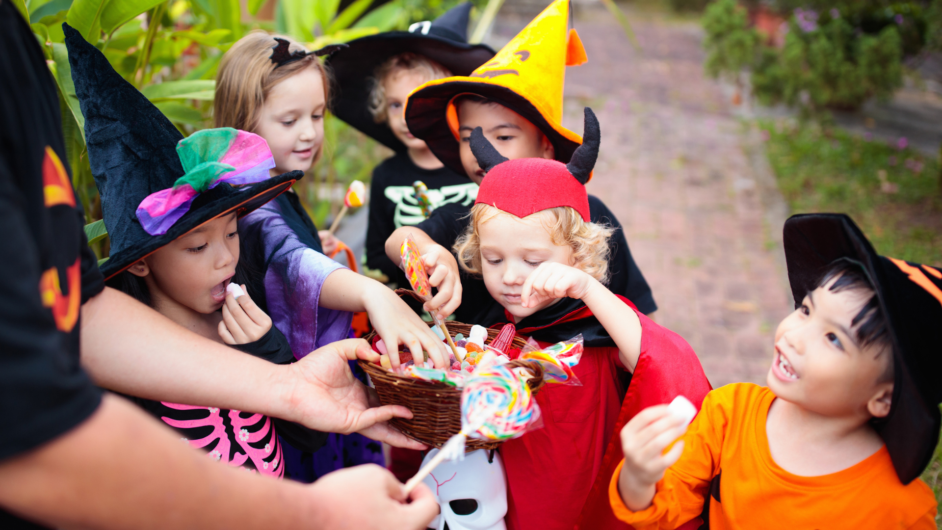 Children in Halloween costumes reaching for candy from a basket held by a person.