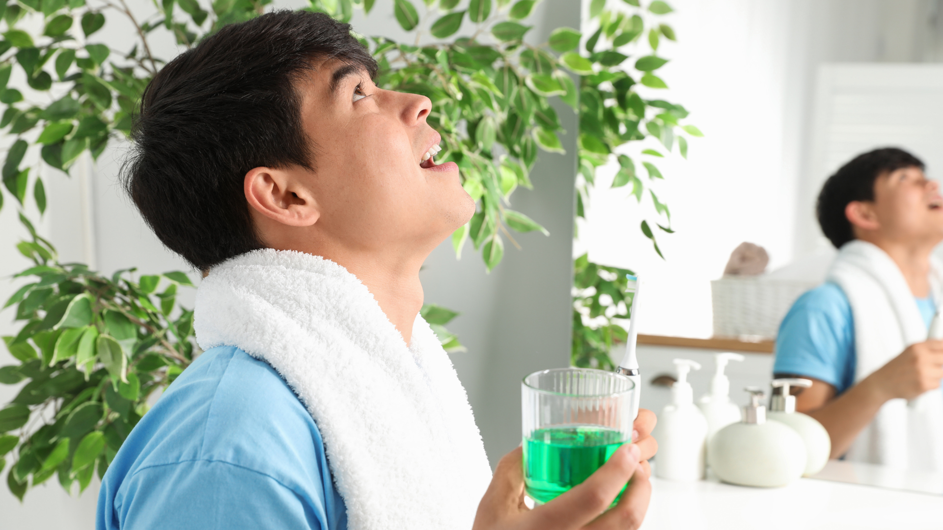 Man rinsing mouth with green mouthwash in a bathroom. Another man in background.