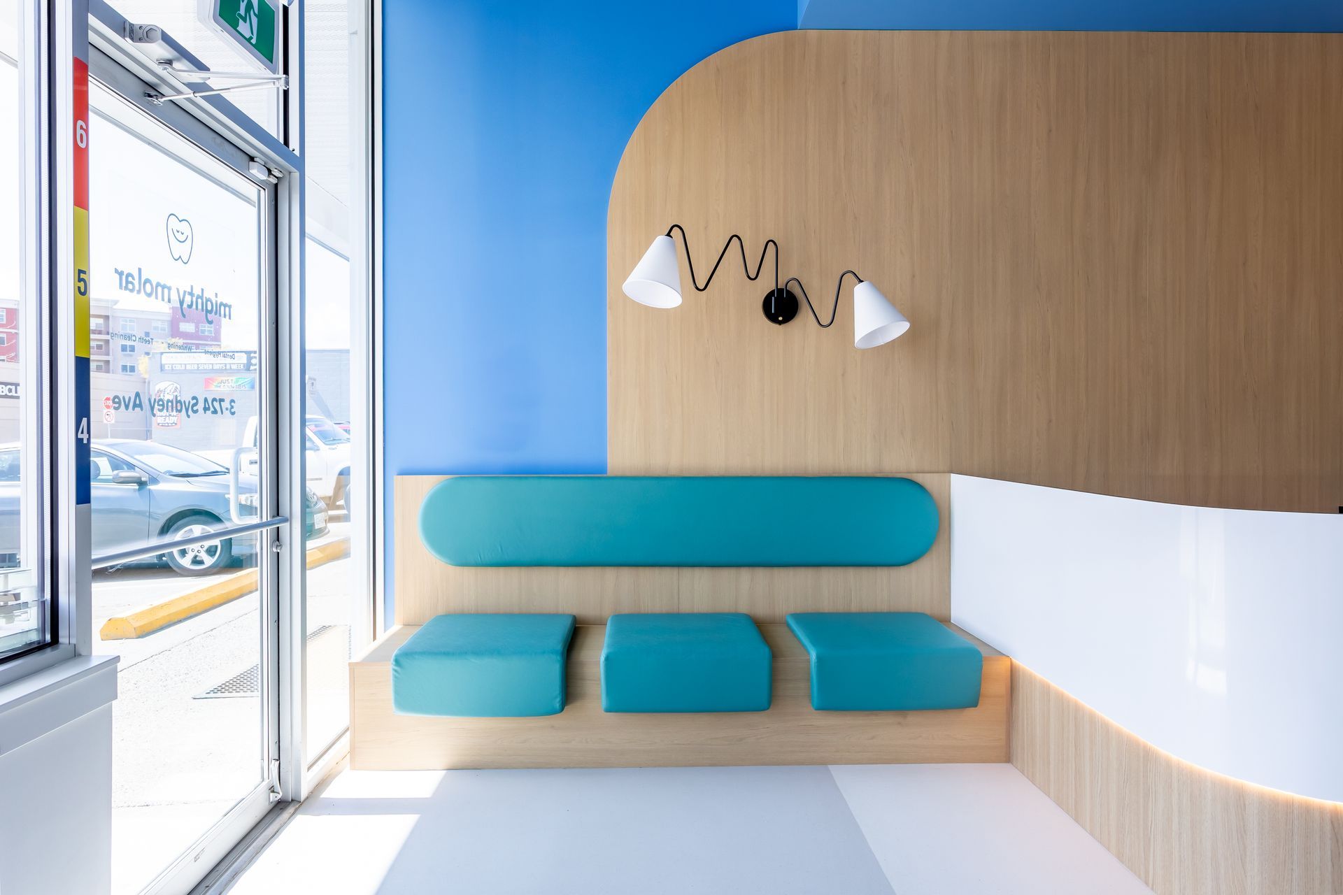 Modern lounge with teal bench seating, wood wall, and pendant lights beside large windows