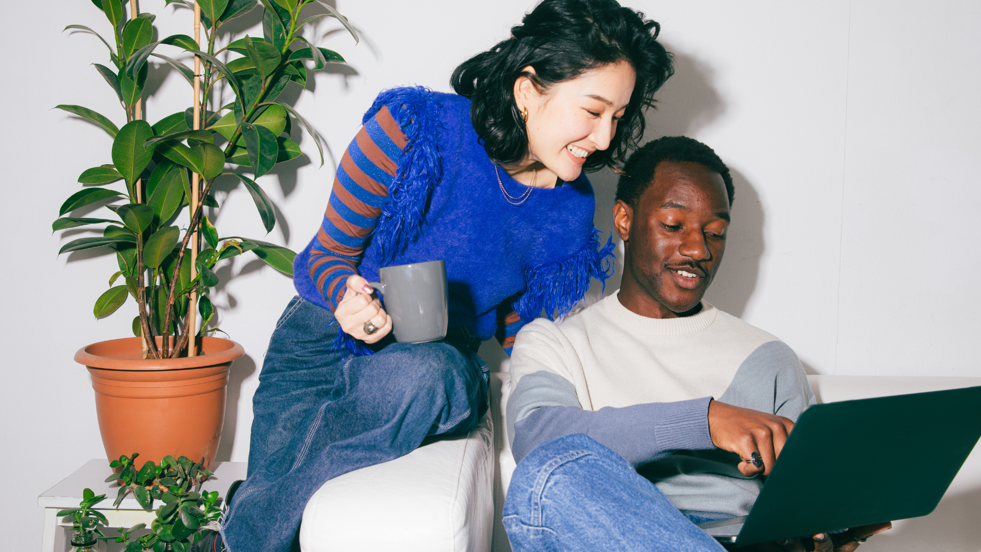 A man and a woman are sitting on a couch looking at a laptop.