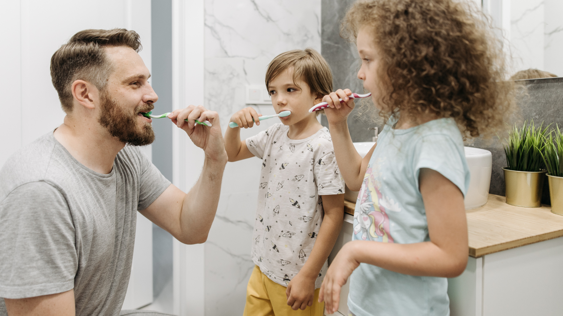 Man and two kids brushing teeth in bathroom.
