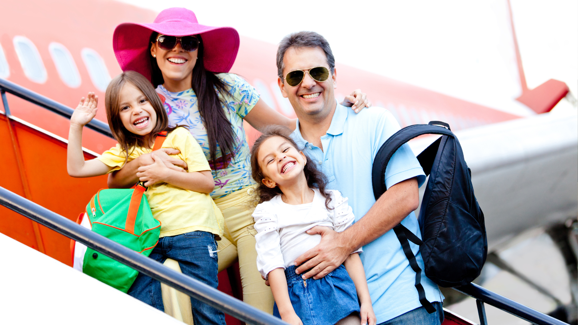 Family smiling and waving on airplane stairs, ready for a trip.