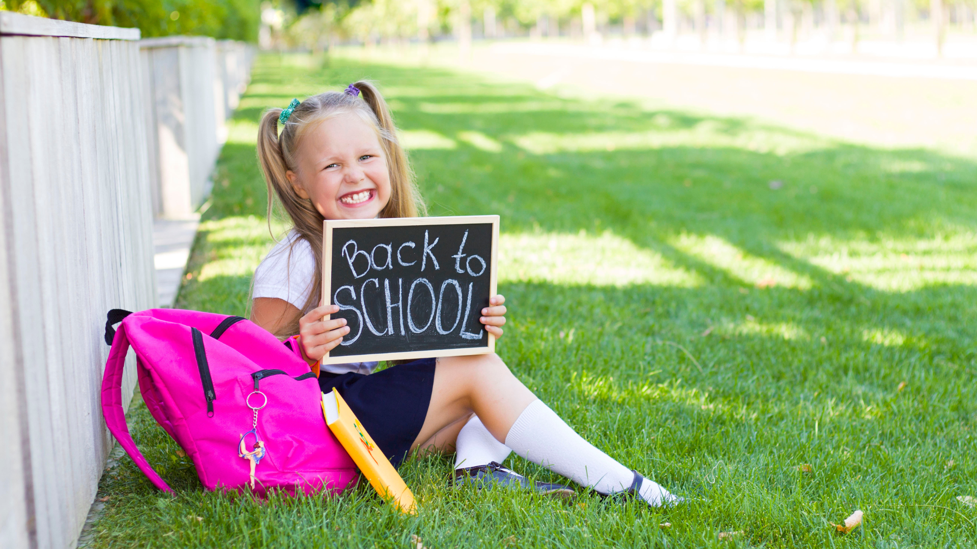 Girl sitting on grass with backpack, holding 