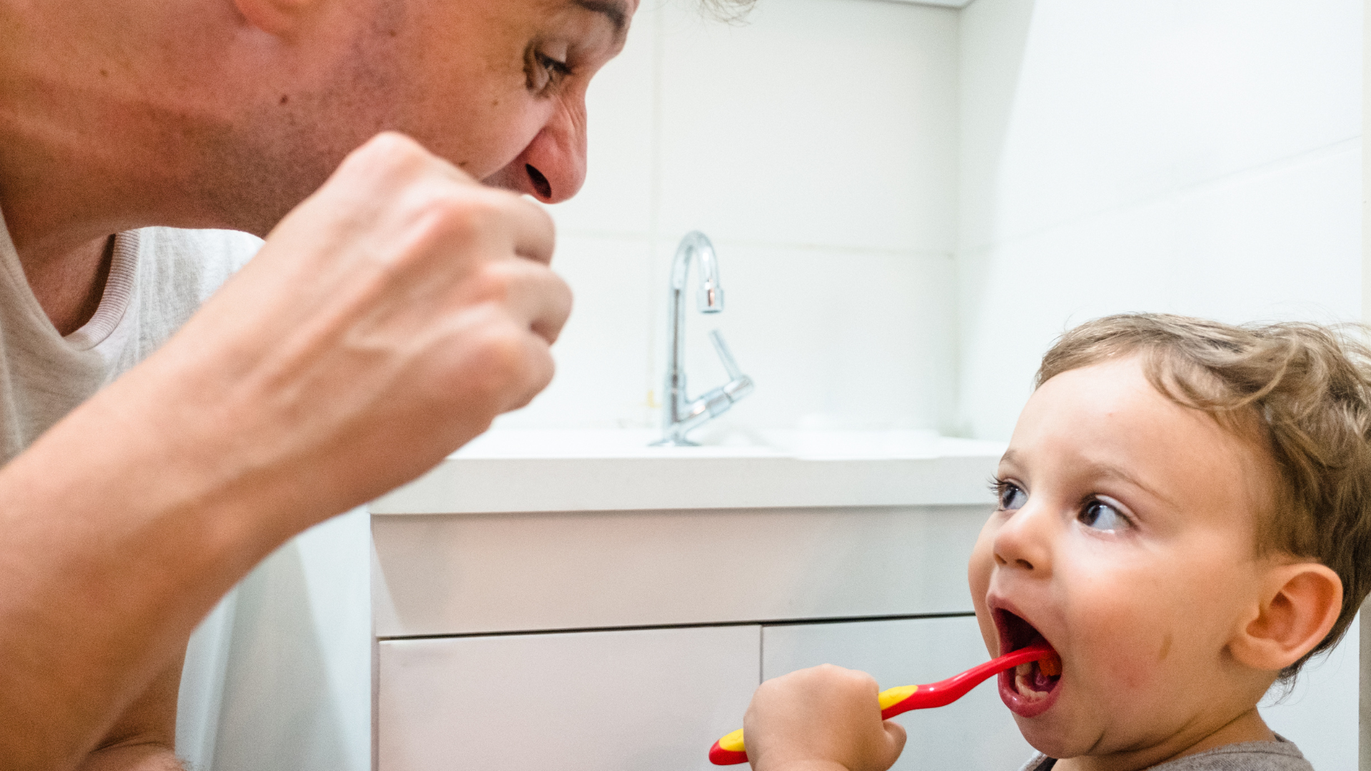 Man and child brushing their teeth together in a bathroom.