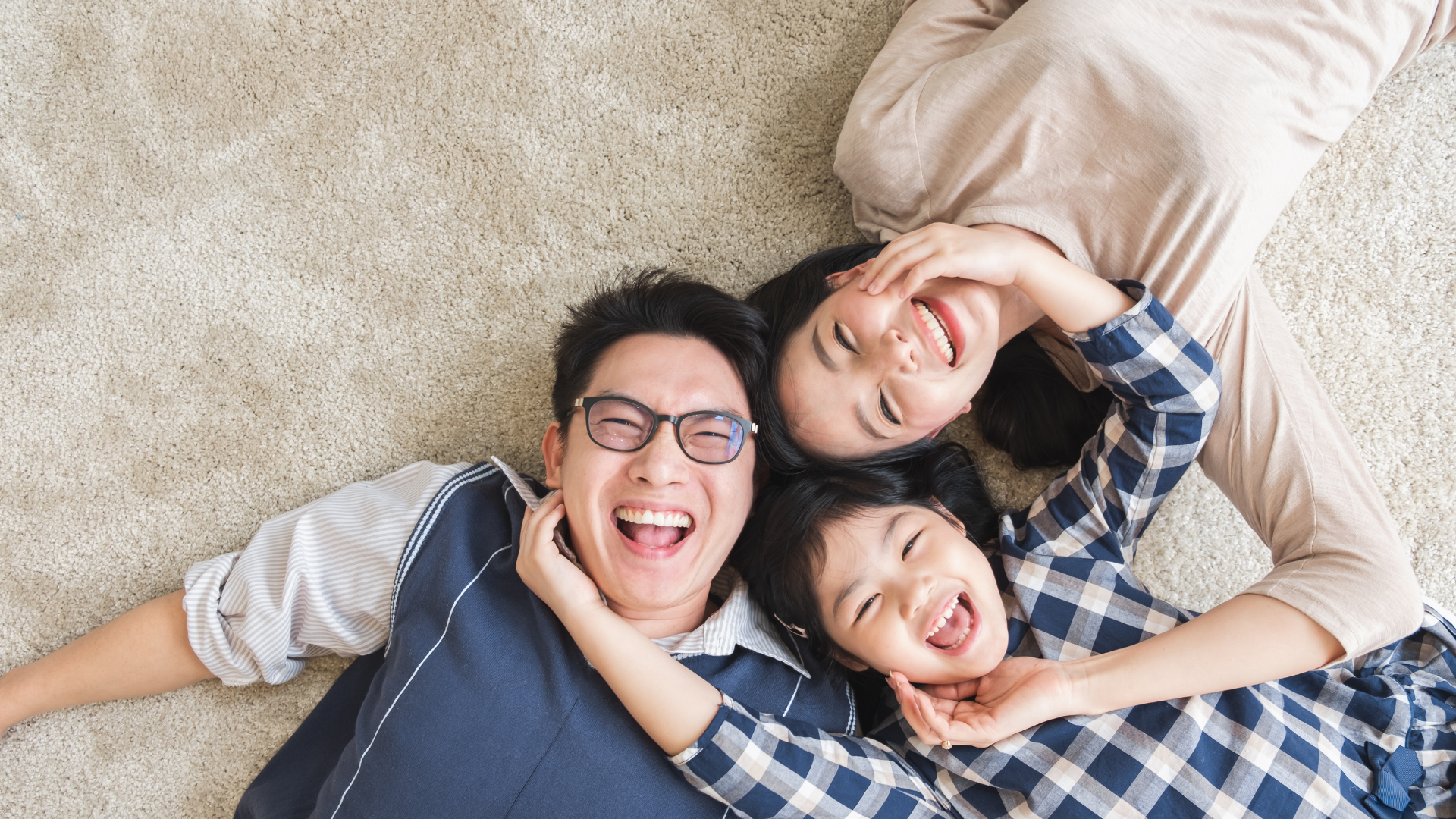 Family lying on a beige carpet, laughing and smiling.