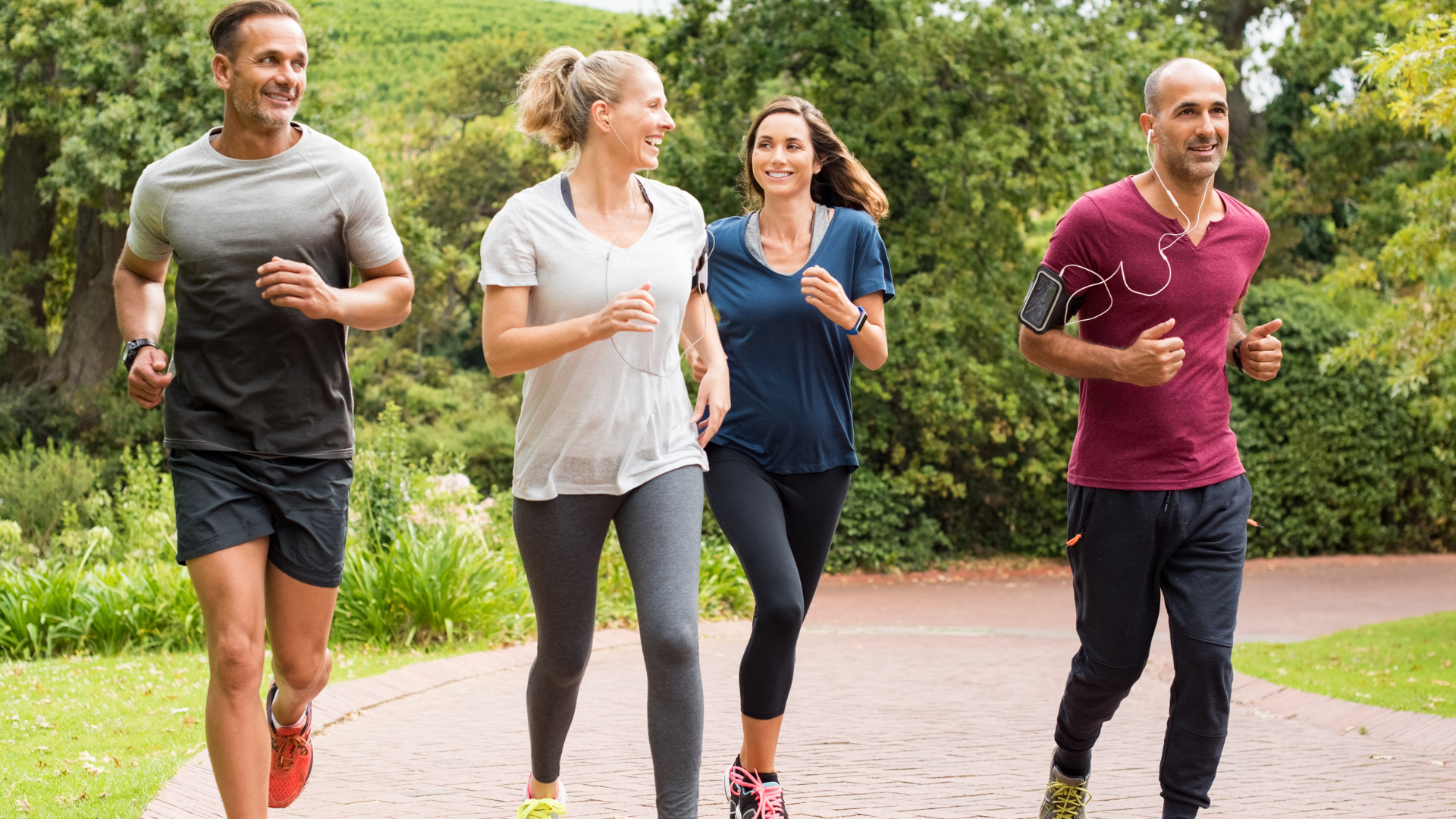 Four people jogging on a paved path in a park with trees in the background.