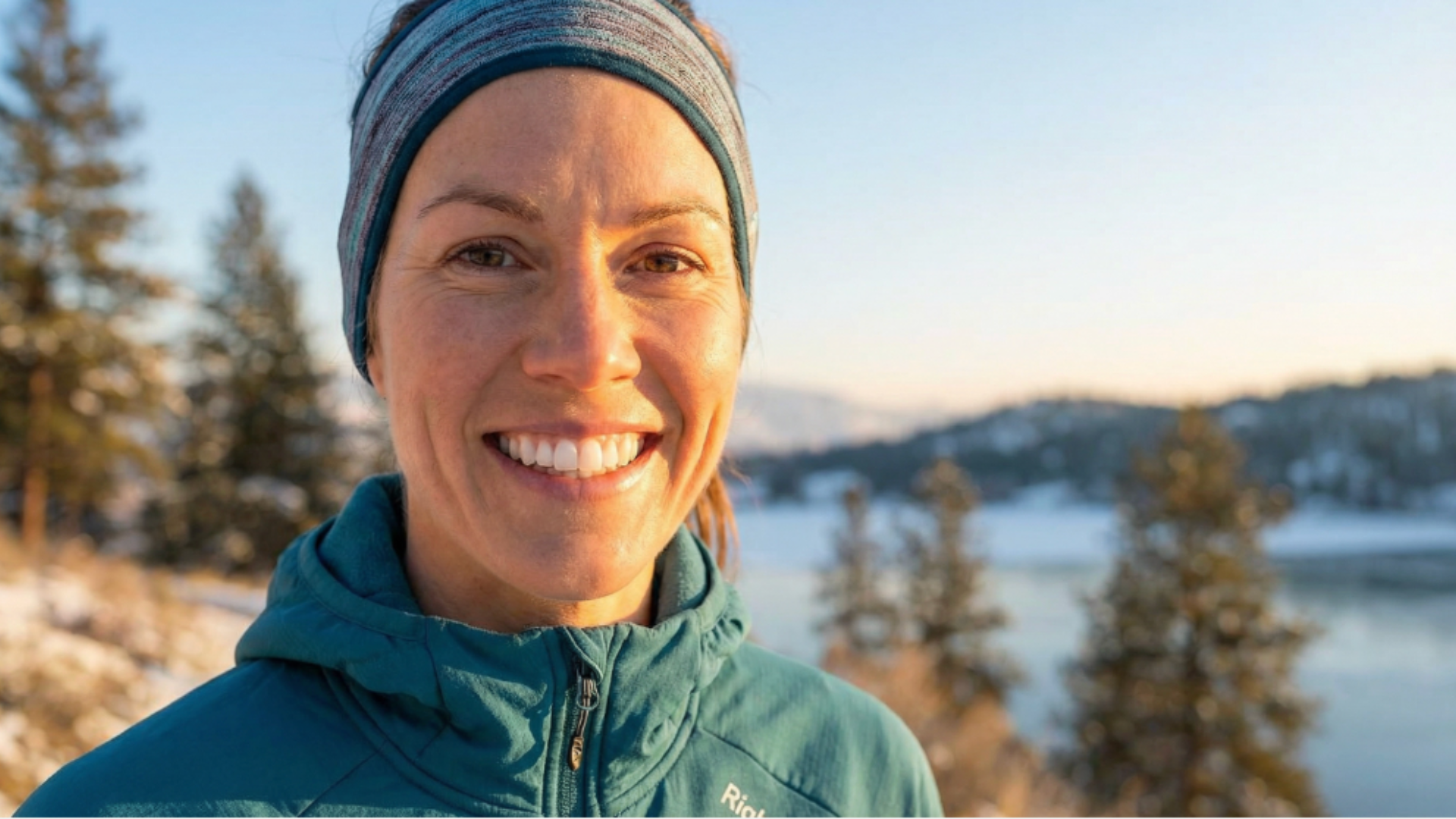 Woman in teal sportswear smiling at camera; snowy landscape in background.