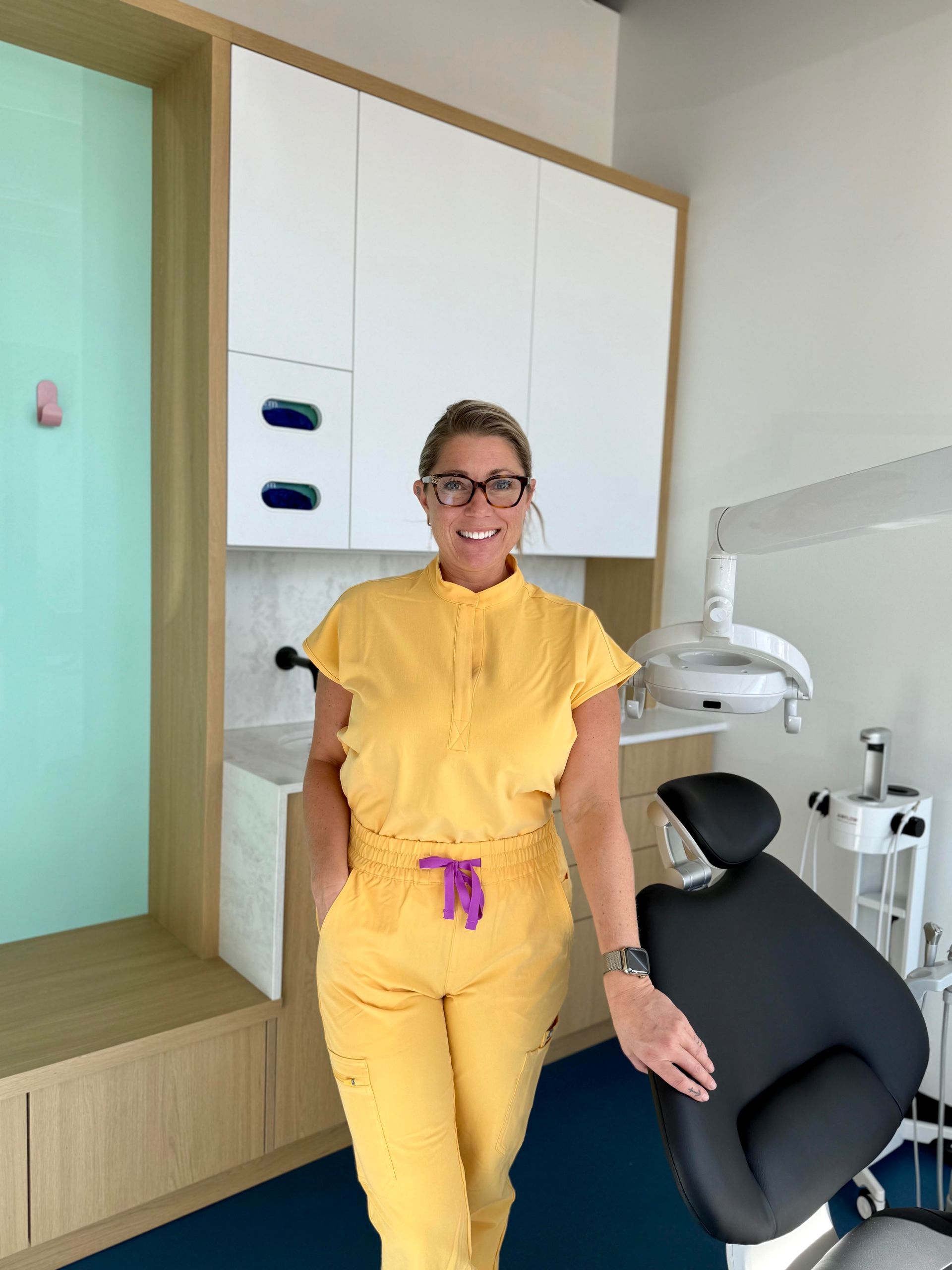 Woman in yellow scrubs stands in a modern dental office.