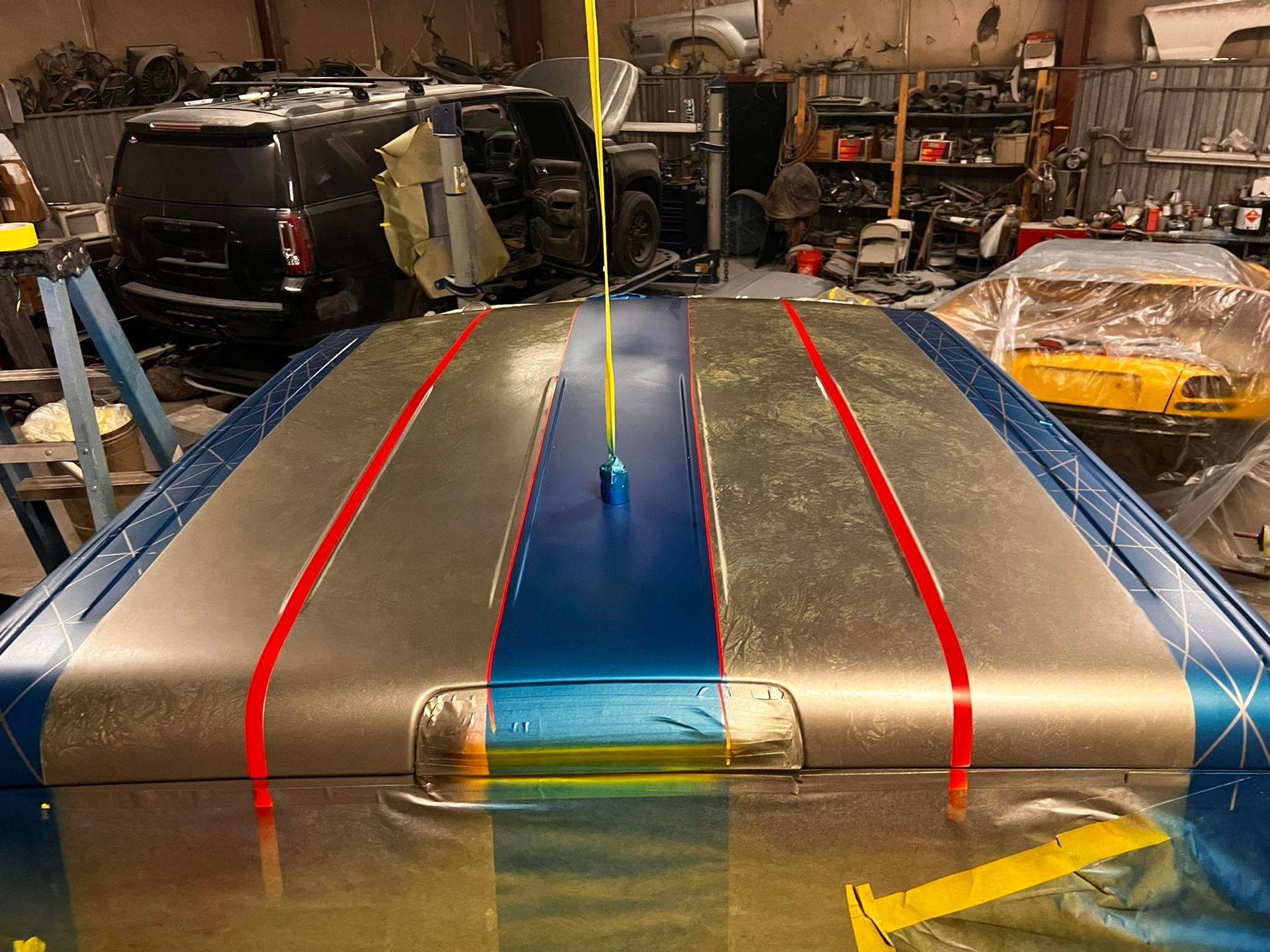 A vehicle roof in a workshop, featuring a metallic silver finish with blue stripes accented by thin red pinstripes.