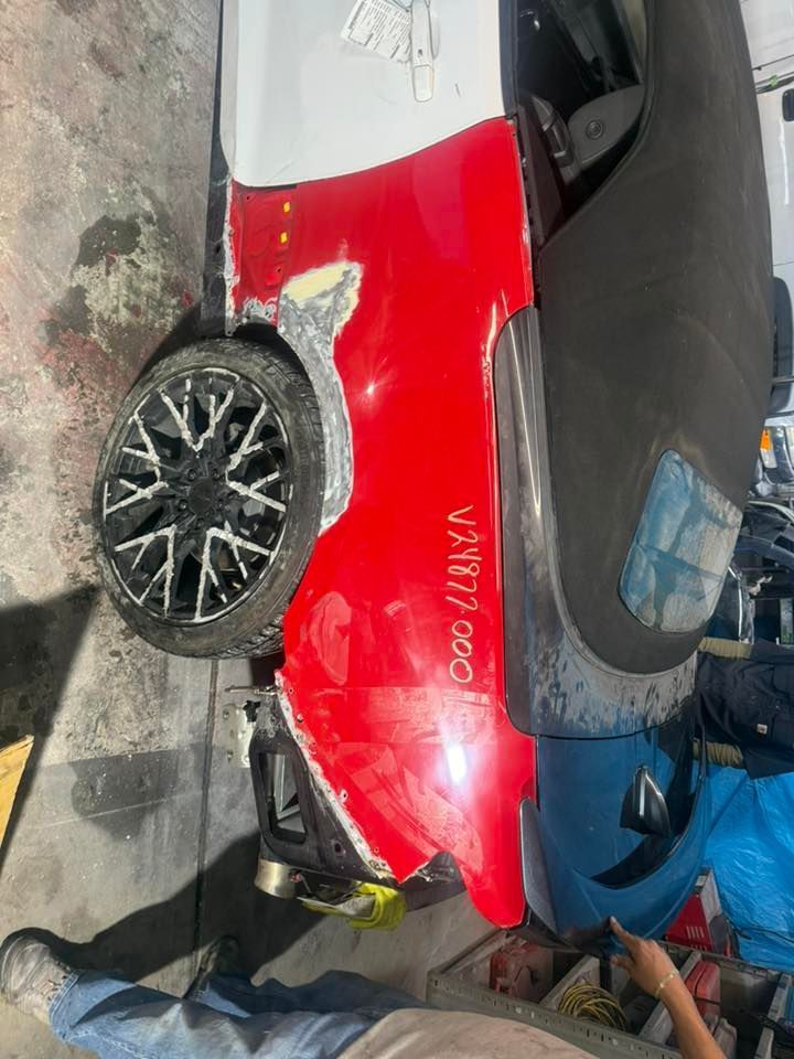 A partially repaired red car body panel showing filler, a black wheel, and a portion of a convertible soft top.