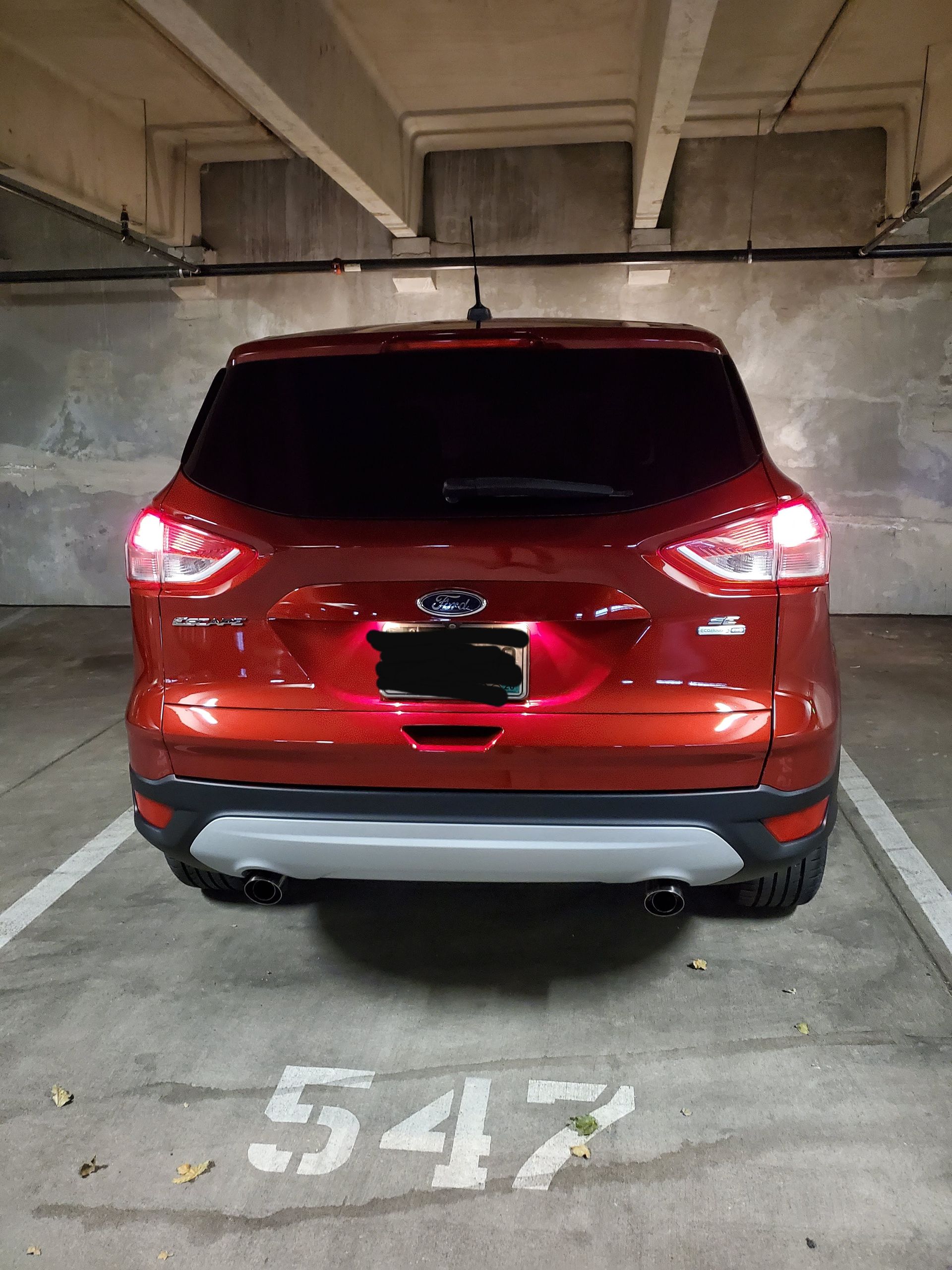 A rear view of a red Ford SUV parked in a concrete parking garage, centered in spot number 547 with its taillights on.