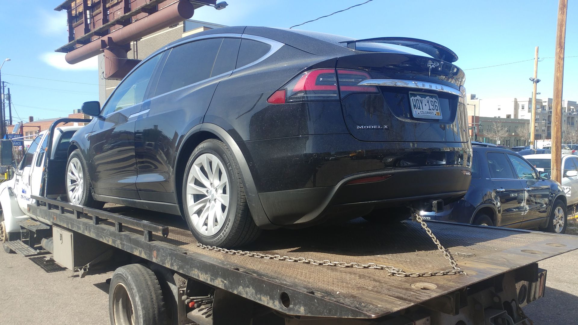 A black Tesla Model X on a flatbed tow truck in an outdoor lot.