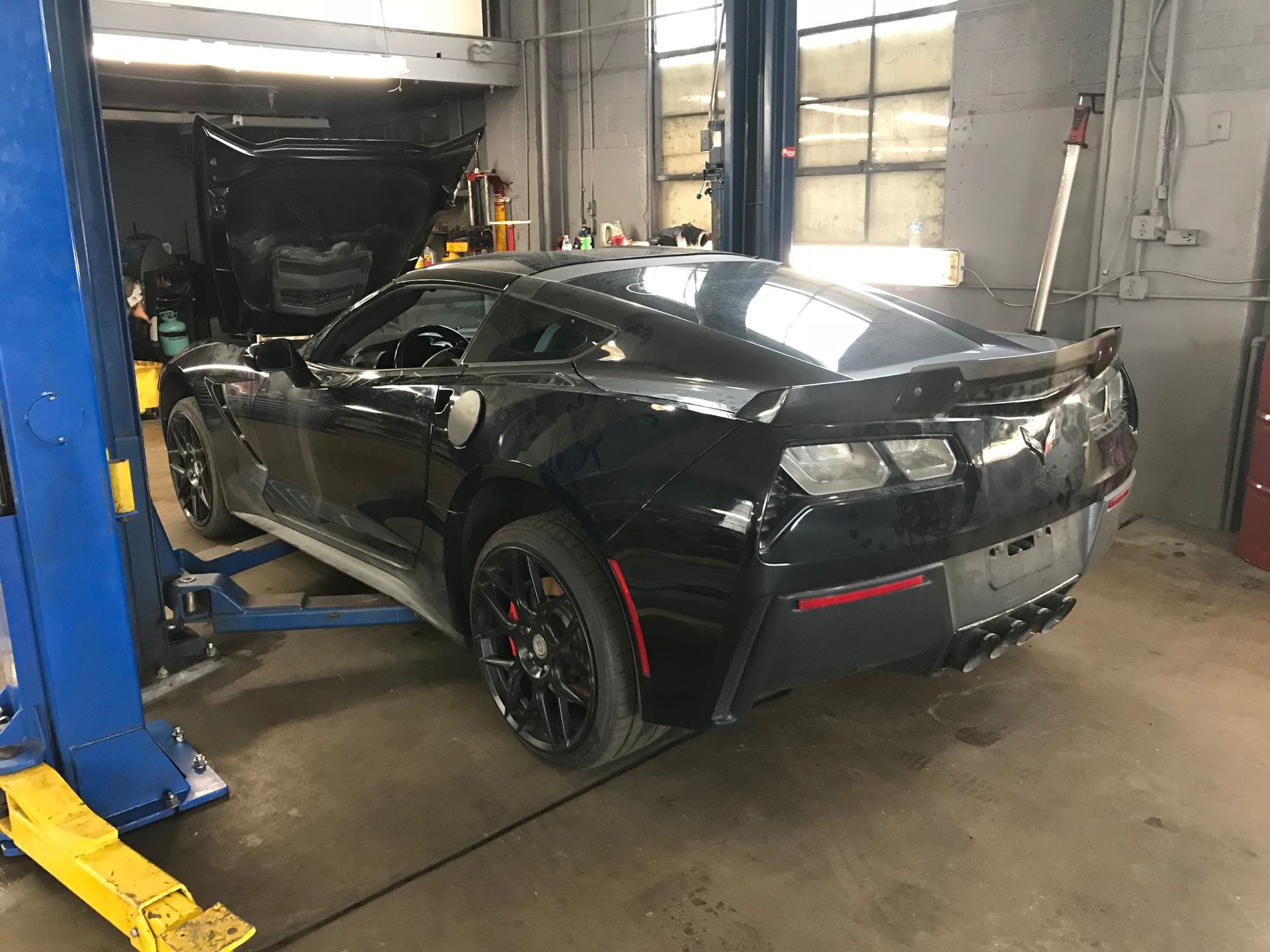 A black Chevrolet Corvette is elevated on a blue hydraulic lift inside a garage for maintenance.