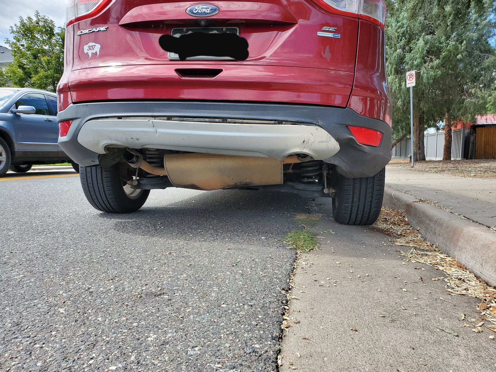 A red Ford Escape parked on the side of a suburban street next to a concrete sidewalk.