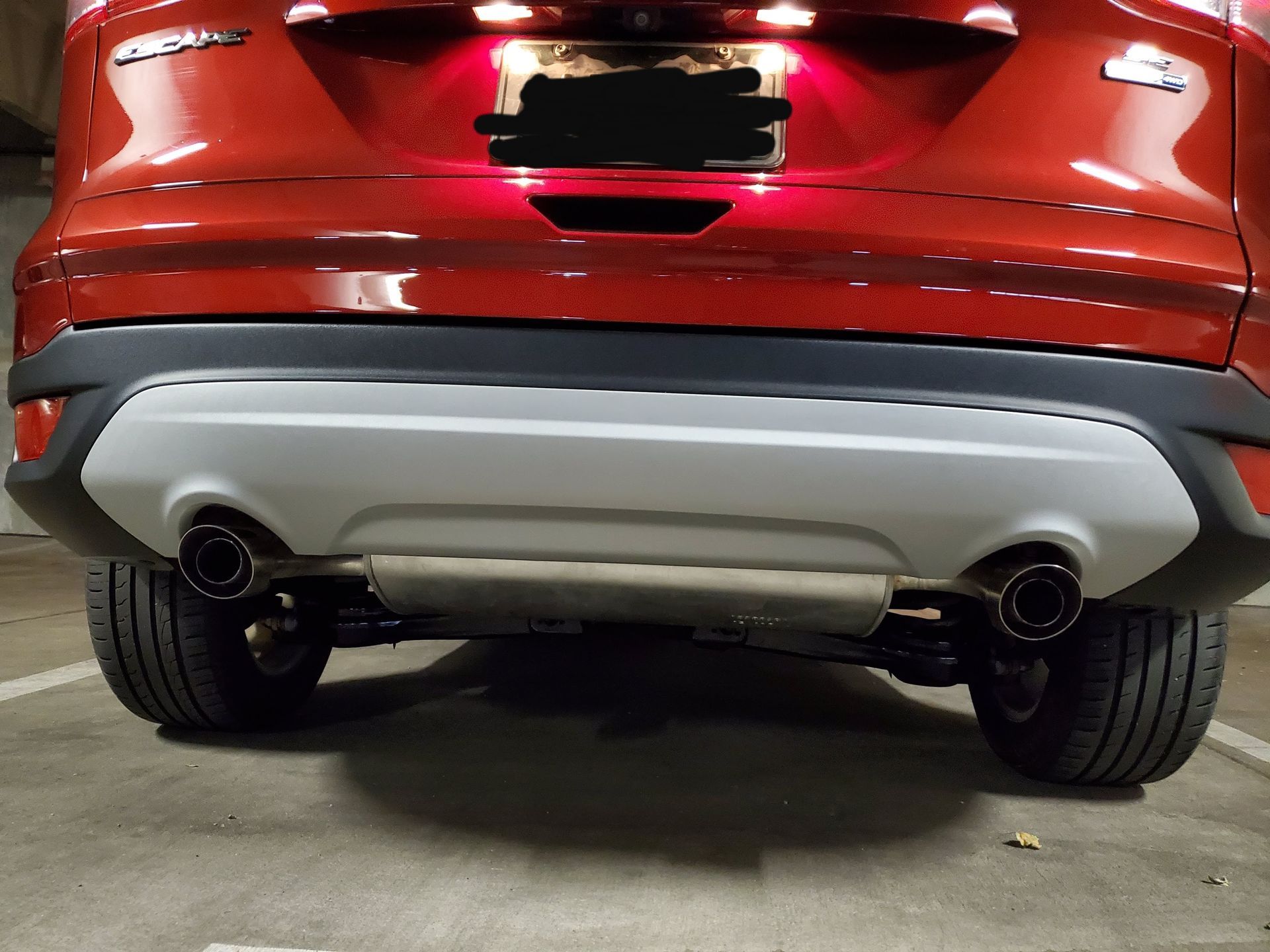 Rear view of a red SUV parked in a garage, focusing on the bumper, exhaust pipes, and silver skid plate.