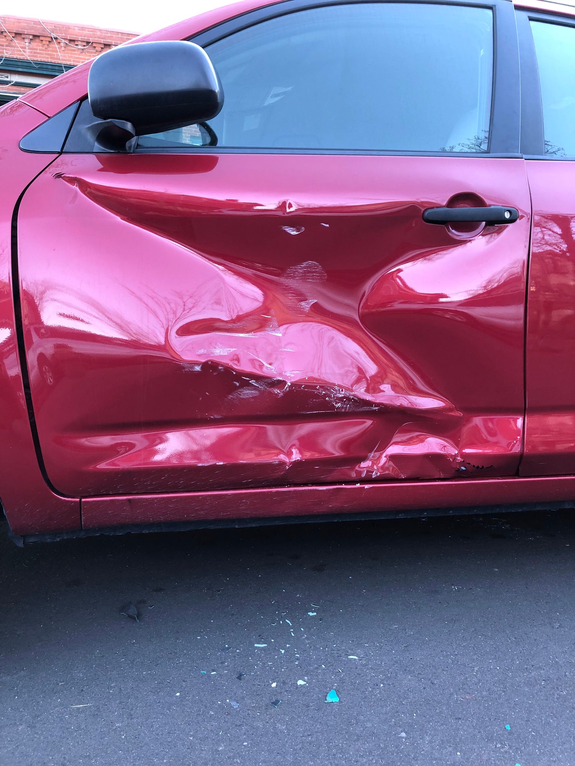 A deep, extensive dent on the passenger side door of a red car, showing damaged metal and paint.