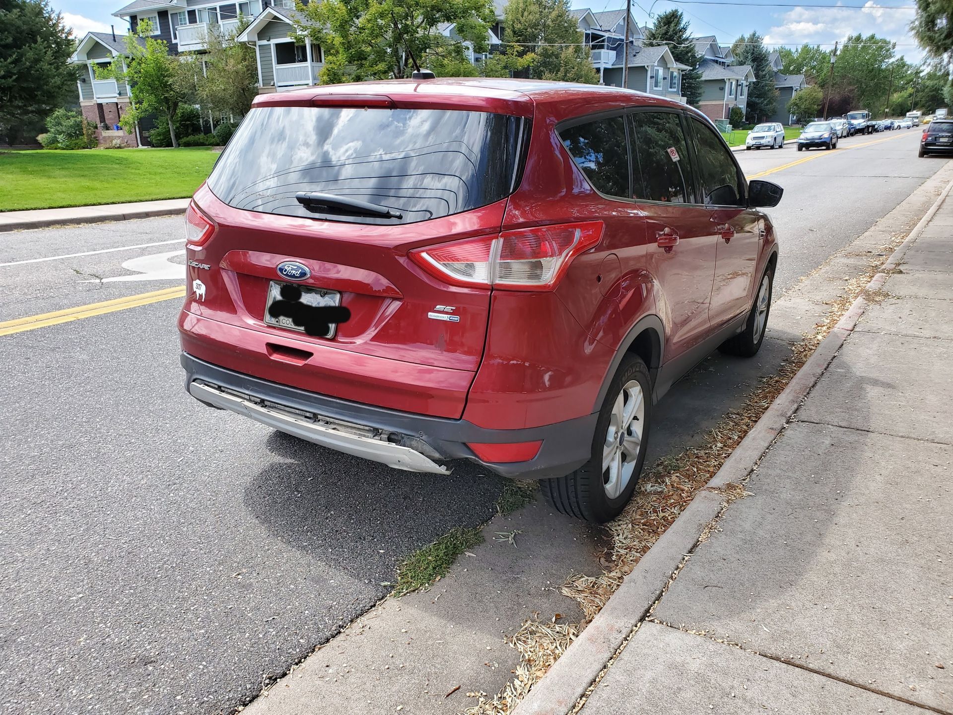A red Ford Escape parked on the side of a suburban street next to a concrete sidewalk.