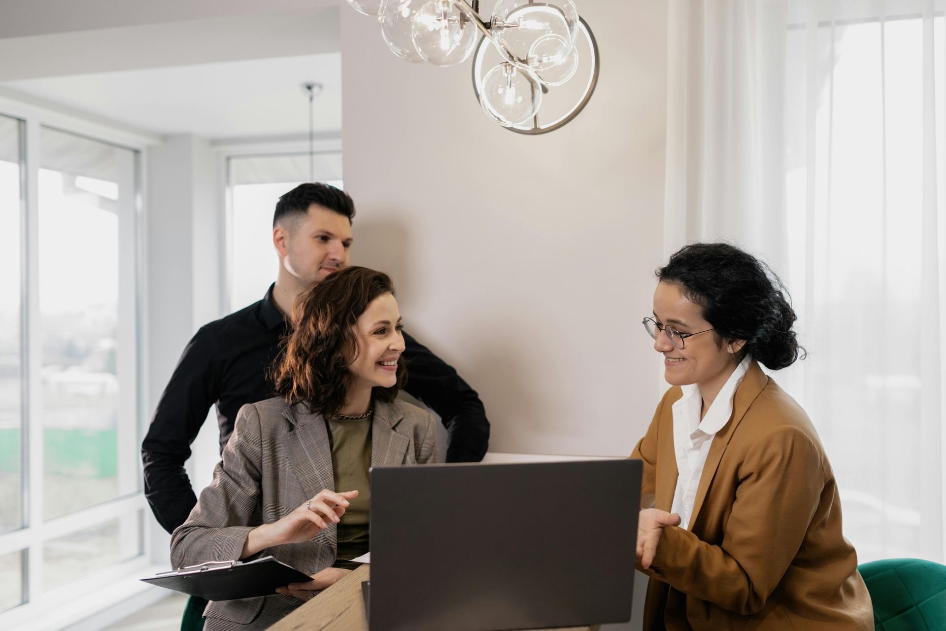 A woman is sitting in front of a laptop computer while a man and woman look on.