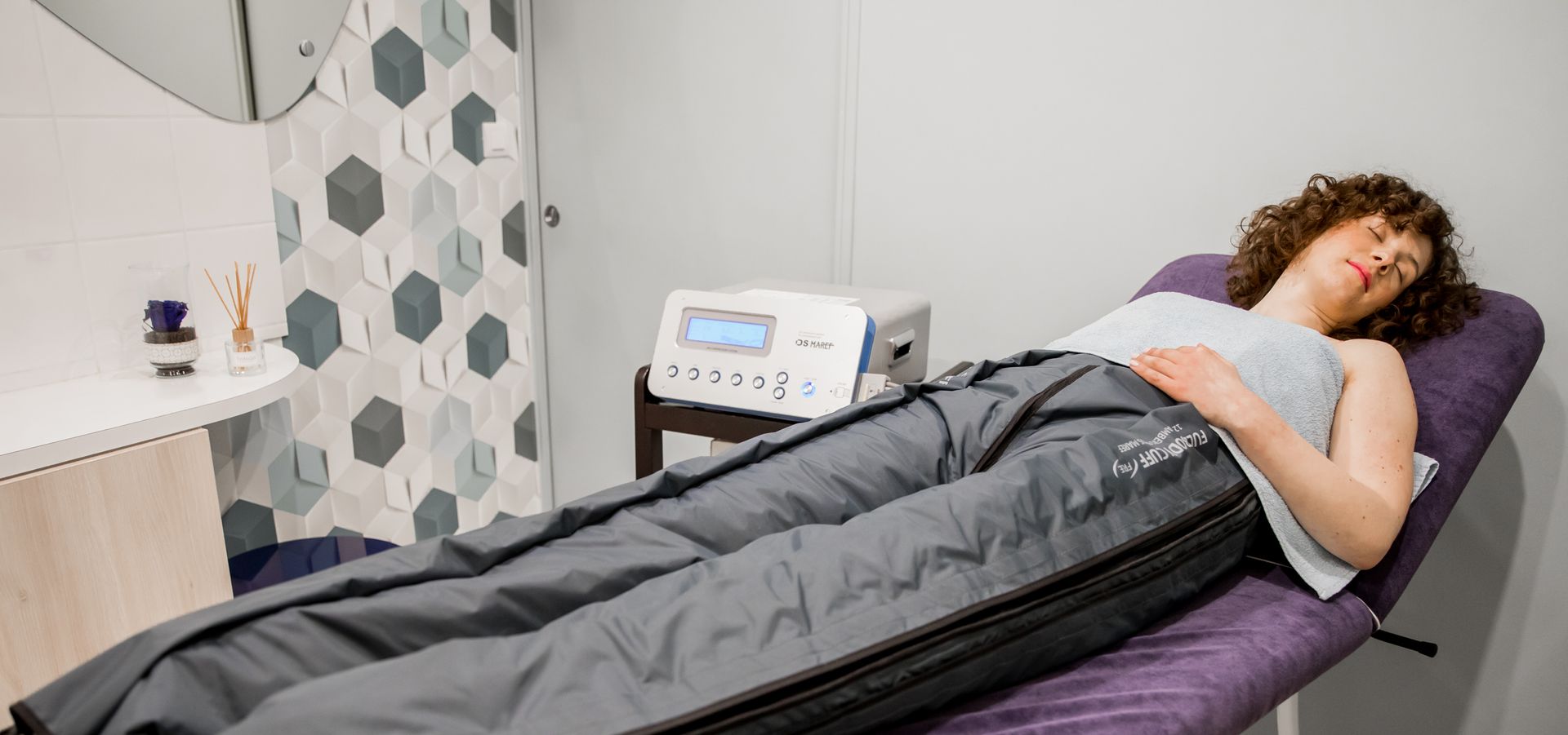 Une femme est allongée sur un lit violet avec un sac de couchage sur son corps.