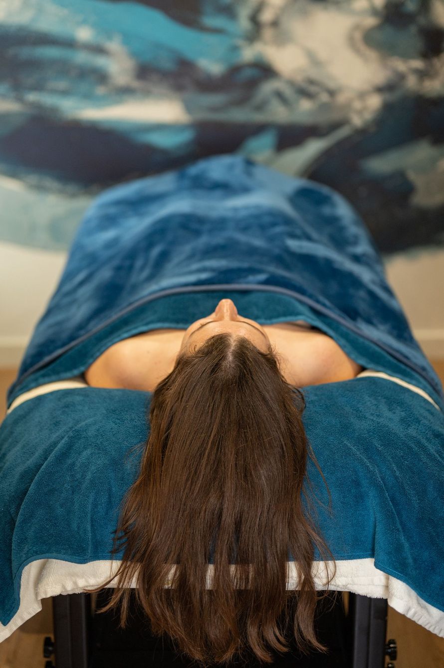 Une femme est allongée sur une table de massage avec sa tête sur une serviette bleue.