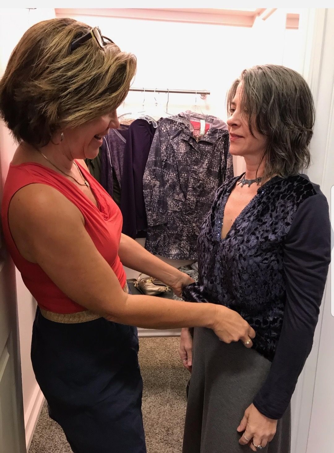 Two women are standing next to each other in a dressing room.