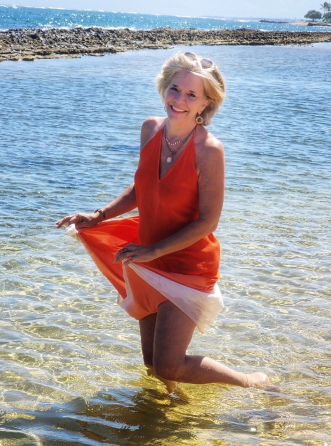 A woman in an orange dress is kneeling in the water
