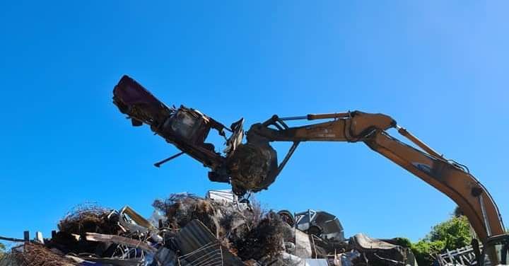 A Large Pile of Scrap Metal is Being Loaded Into a Truck by an Excavator — Hastings Scrap Metal Recyclers in Wauchope, NSW