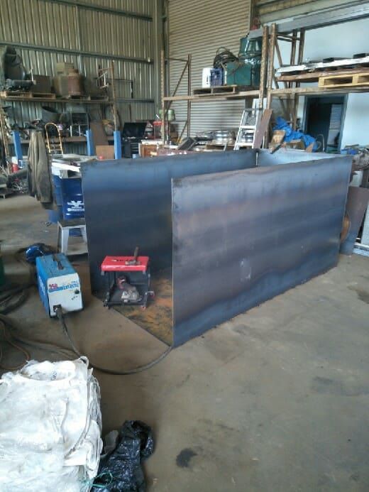 A Large Piece of Metal is Sitting in a Warehouse Next to a Welding Machine — Hastings Scrap Metal Recyclers in Wauchope, NSW