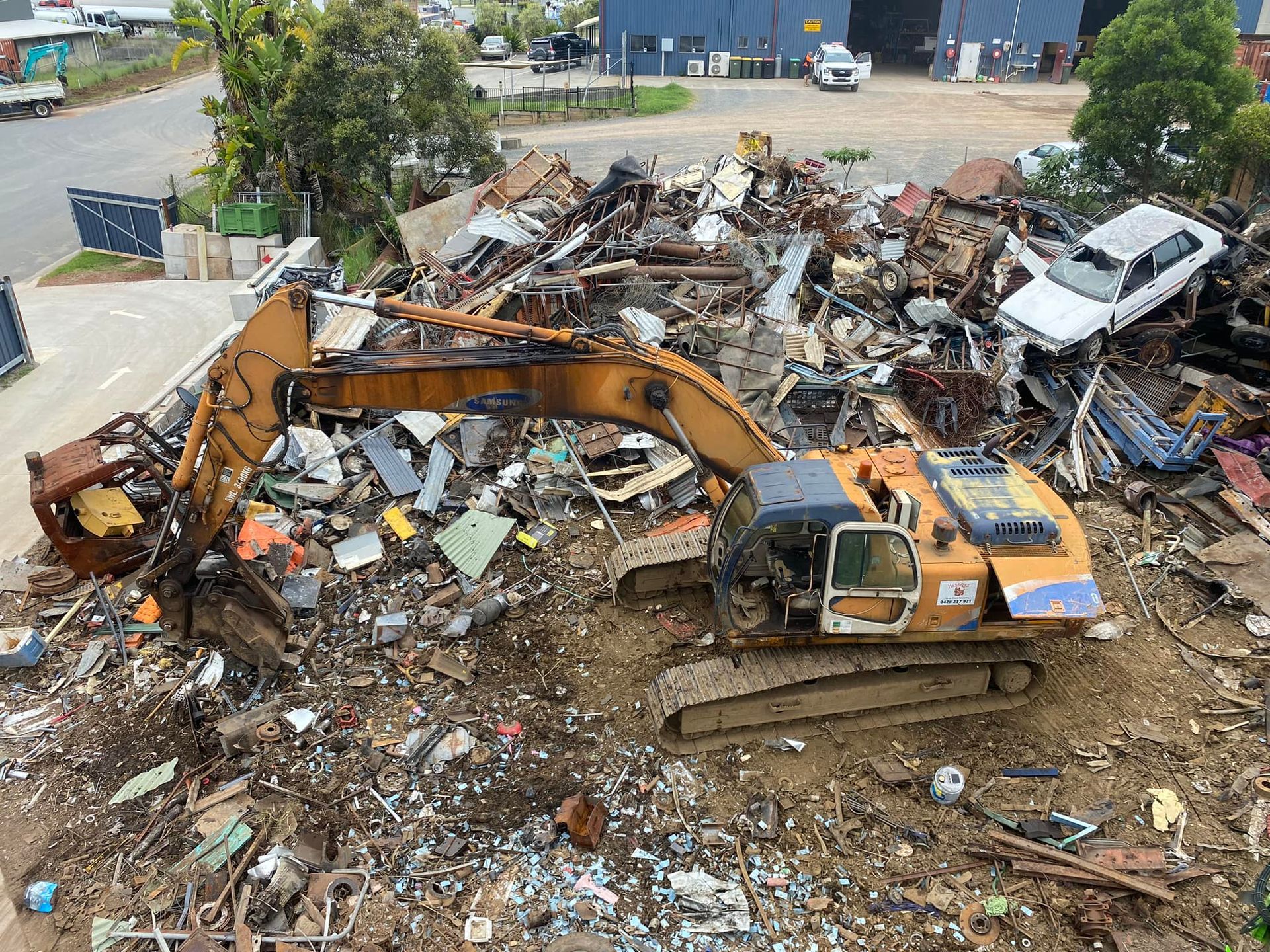 A Large Pile of Scrap Metal is Being Loaded Into a Truck by an Excavator — Hastings Scrap Metal Recyclers in Wauchope, NSW