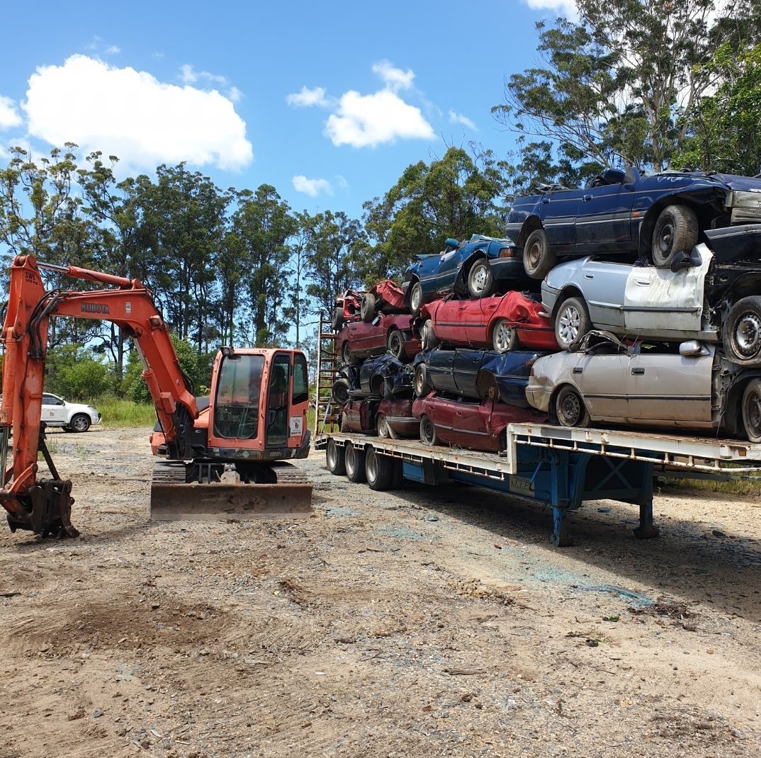 An Excavator with Piles of smashed Cars Stacked on Top of Each Other On A Trailor— Hastings Scrap Metal Recyclers in Kempsey, NSW