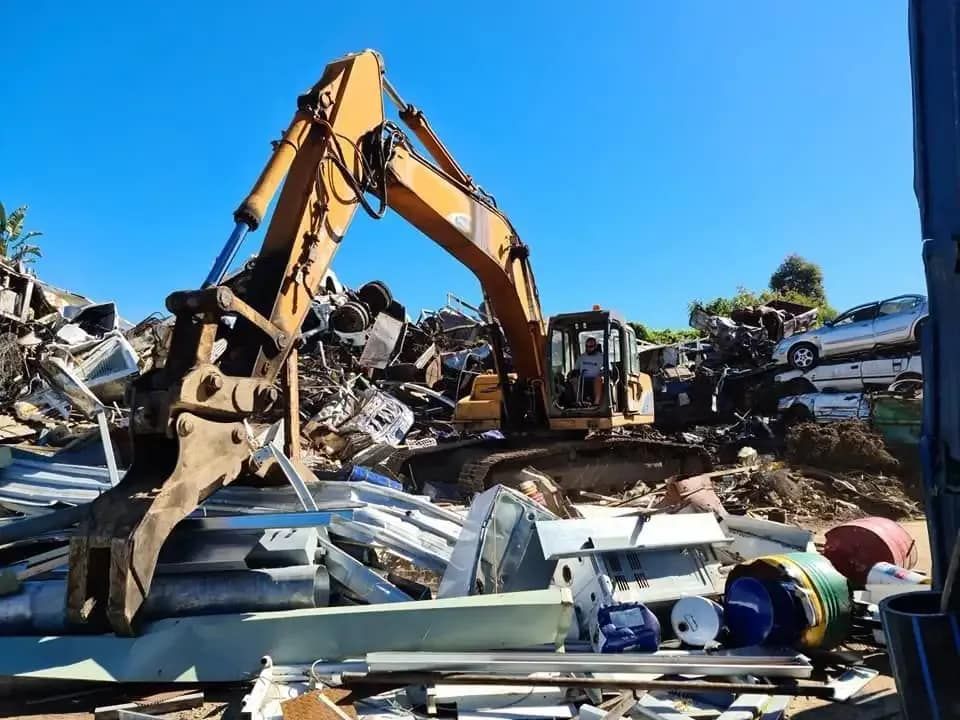 A Yellow Excavator is Working on a Pile of Scrap Metal — Hastings Scrap Metal Recyclers in Kew, NSW