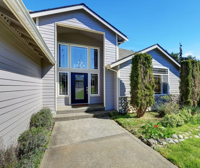 A gray house with a blue door and a concrete walkway leading to it.