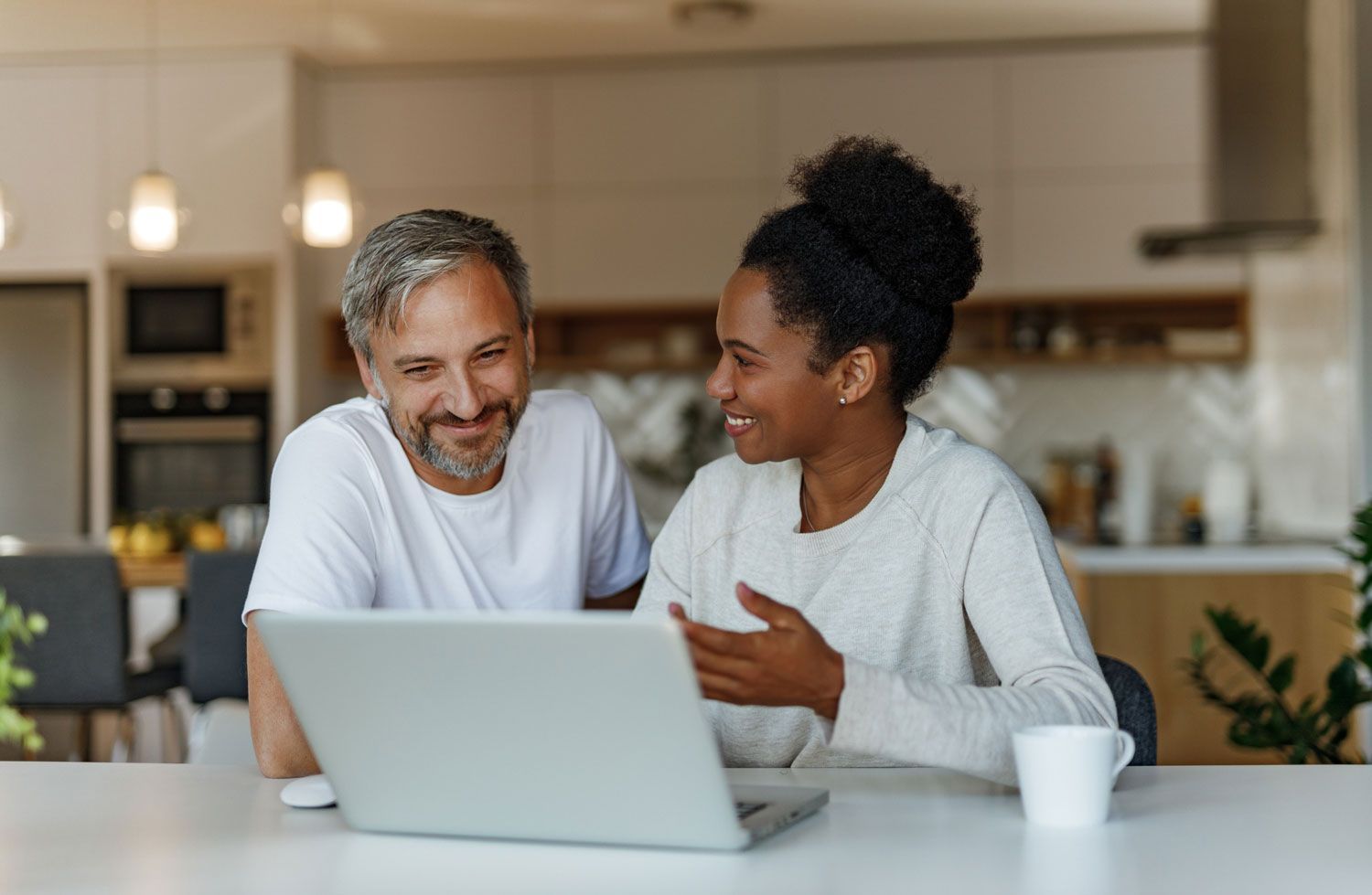 A man and a woman are sitting at a table looking at a laptop computer.