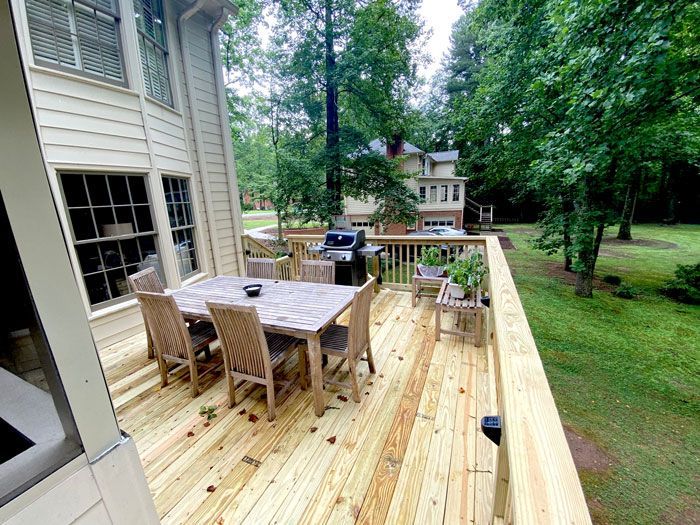 A wooden deck with a table and chairs and a grill.