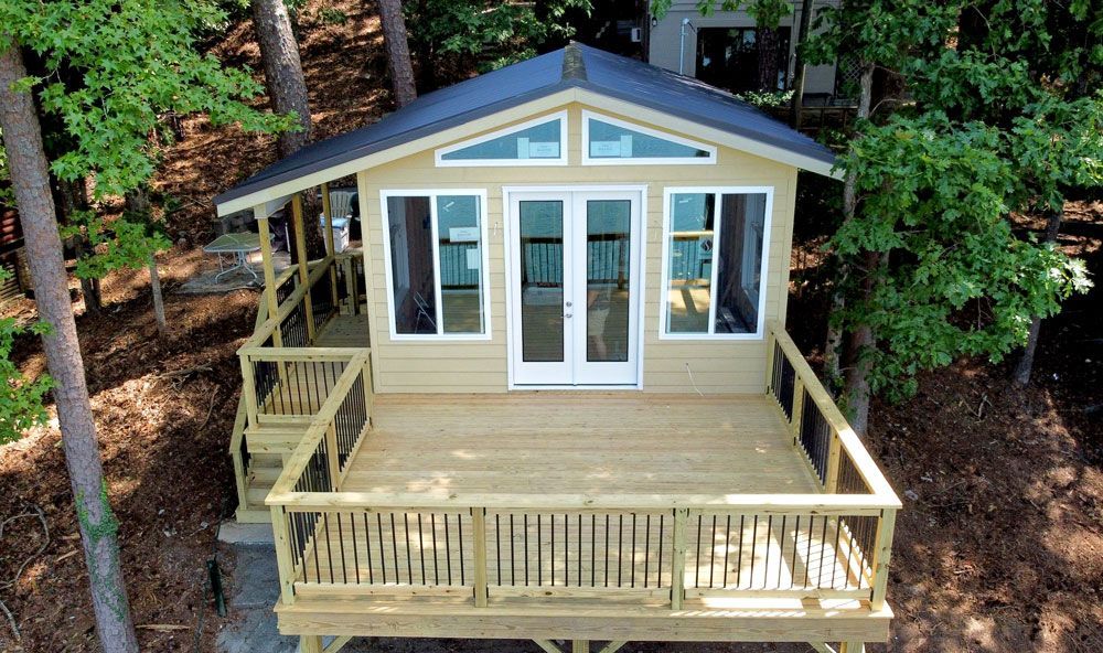 An aerial view of a small house with a deck in the middle of a forest.