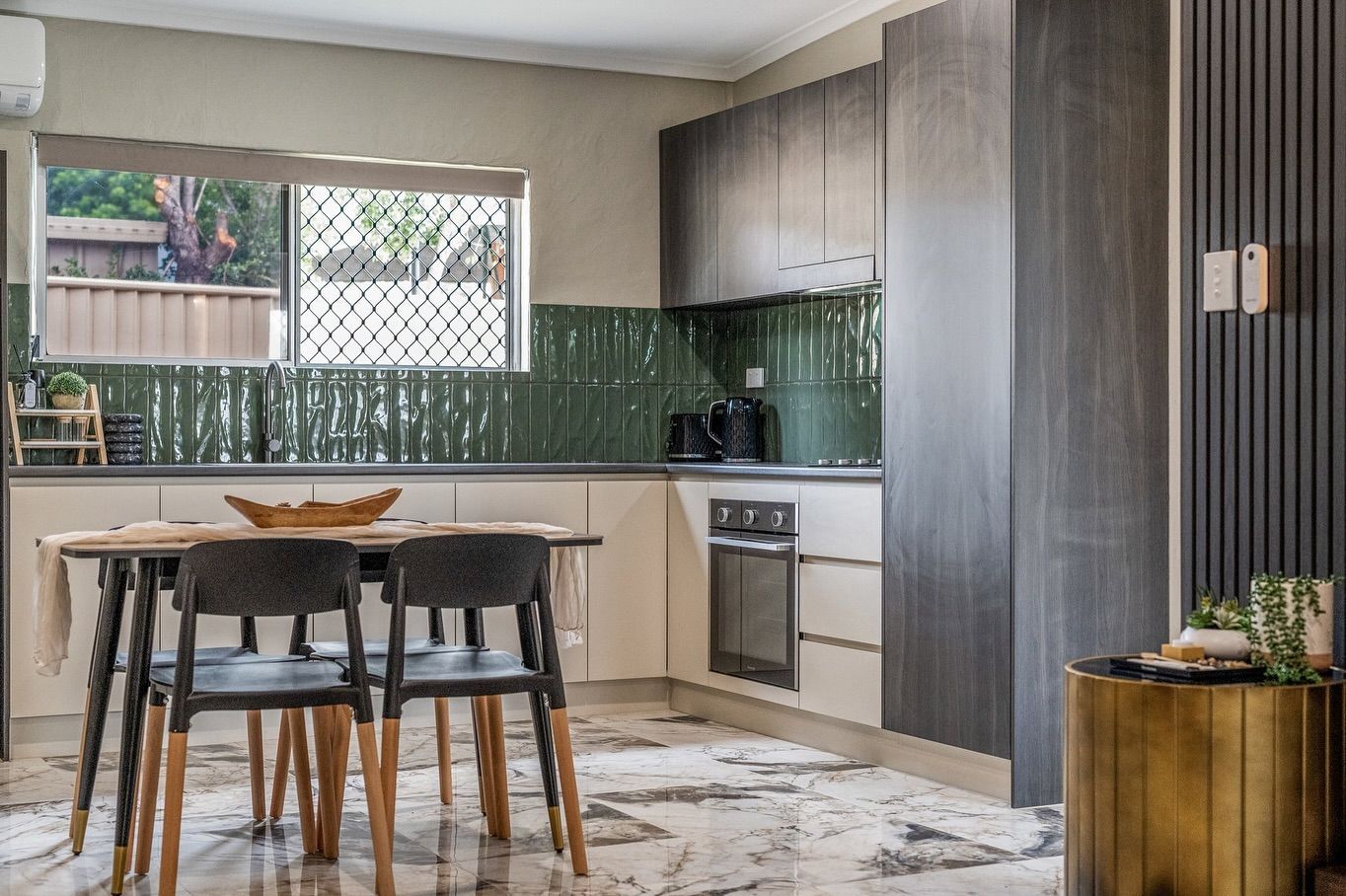 Kitchen with dark wood cabinets, green tile backsplash, table with chairs, and marble floor — Cooloola Tile Company in Gympie, QLD