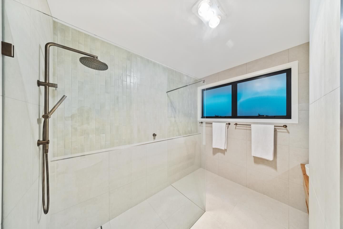 Shower with glass enclosure, rain shower head, window with blue view, and white towels - Cooloola Tile Company, Gympie