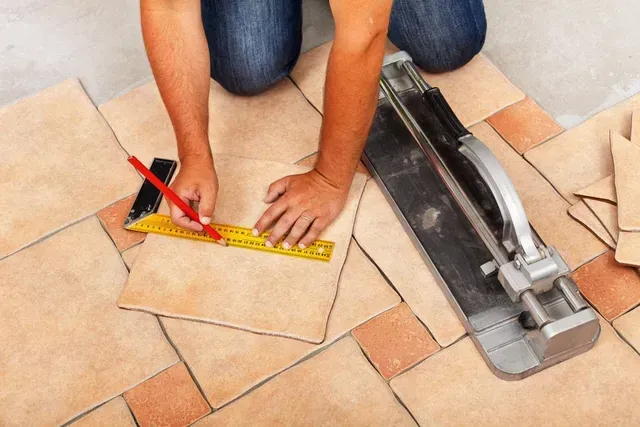 Person Kneeling, Measuring Tile With Ruler and Pencil, Near Tile Cutter — Cooloola Tile Company in Hervey Bay, QLD