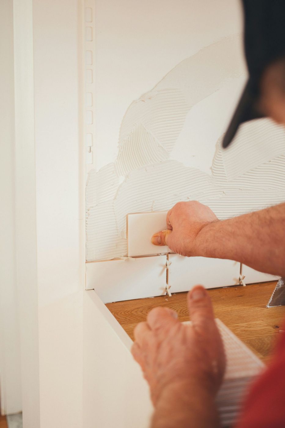 Person Installing White Tiles on a Wall With Mortar, Using a Spacer — Cooloola Tile Company in Gympie, QLD