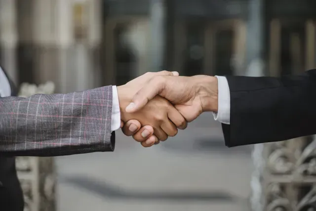 Two men in suits are shaking hands in front of a building.