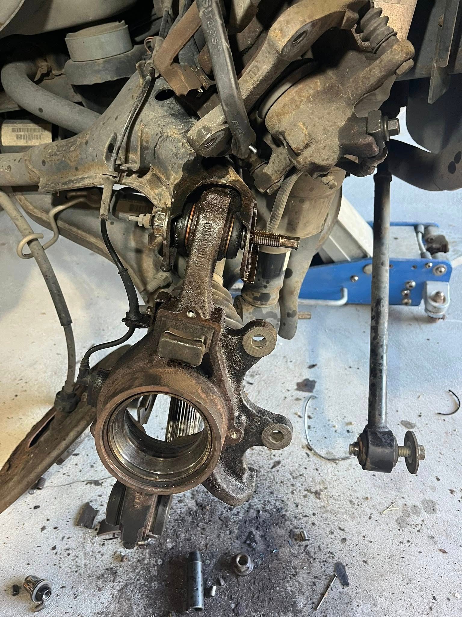 Close-up view of a disassembled, grease-covered automotive wheel hub assembly and suspension components on a garage floor.