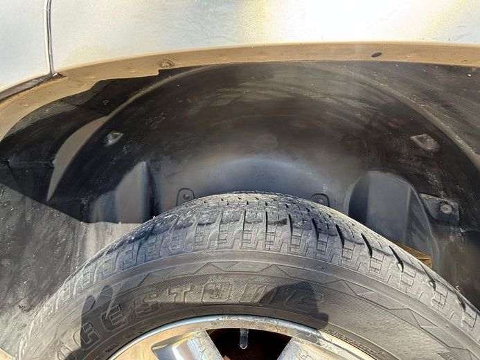 A close-up view of a car's black plastic wheel well liner above a worn, treaded tire.
