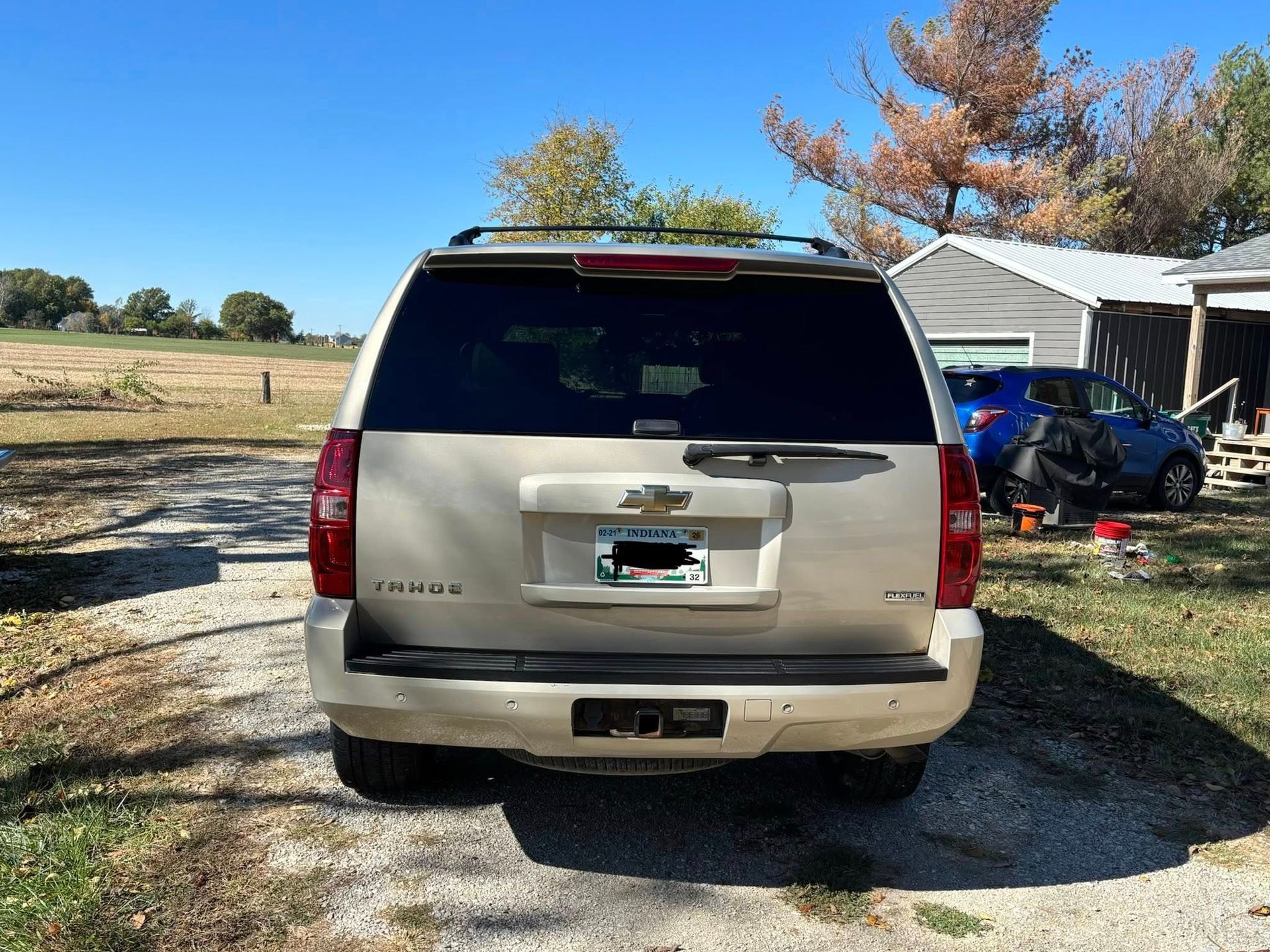 A gold Chevrolet Tahoe parked on a gravel path near a house on a sunny day.