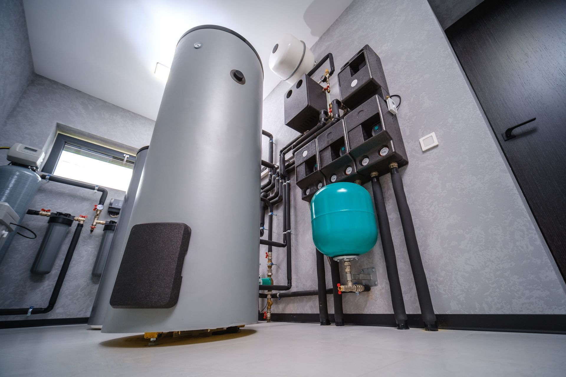 Industrial water heater and plumbing system in a utility room, with a blue expansion tank and pipes.